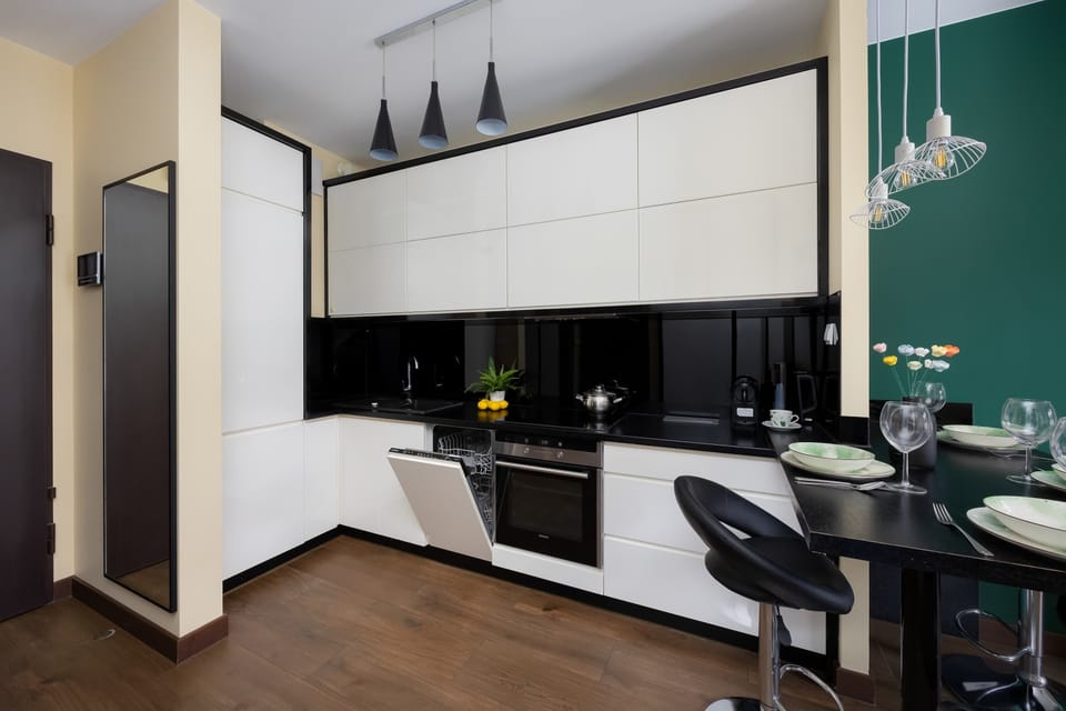 A spacious kitchen layout with white cupboards arranged in an L-shape and dark countertops. Warm wood flooring balances the monochrome design.