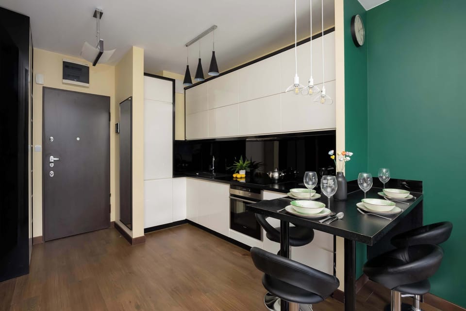 A dining and kitchen area with black chairs, decorative table settings, and sleek cabinetry. The dark entrance door contrasts with the lighter interior palette.