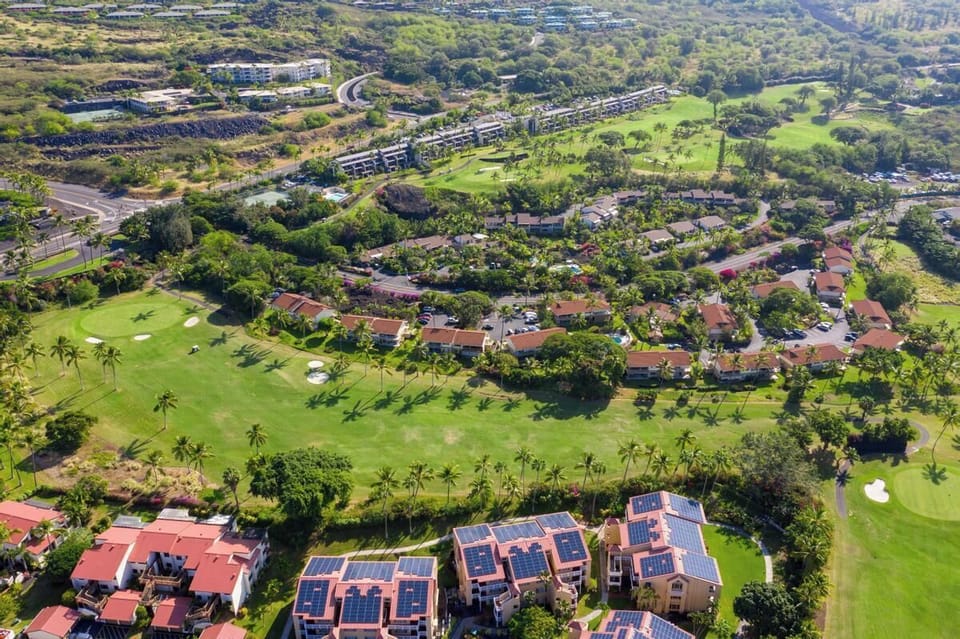 Aerial view of a tropical resort community surrounded by lush golf courses, palm trees, and mountain-backed landscape.