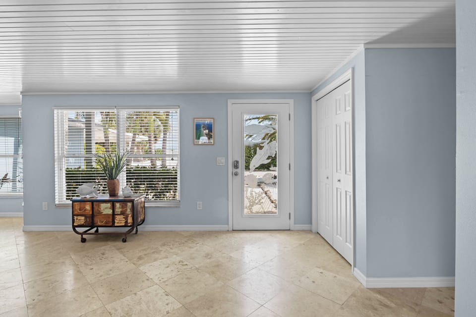 The entrance opens to coastal elegance—neutral tones, natural light streaming through palm-lined windows, and a breezy, welcoming vibe perfect for your beach escape.