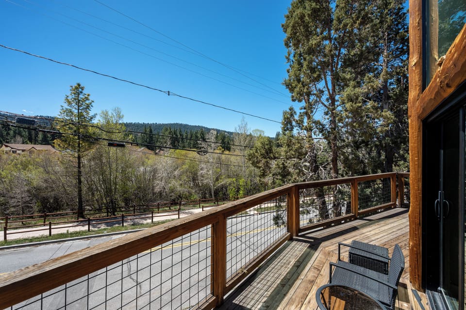 A peaceful street borders the property, framed by towering evergreens and rolling mountains under a clear blue sky, offering a scenic and tranquil mountain neighborhood setting.