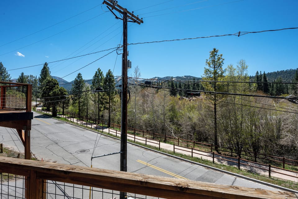 Mountain landscape view from property balcony overlooking wooded hillsides and a quiet residential street, with seasonal spring foliage beginning to bloom.