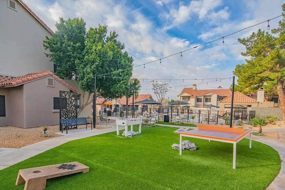 Vibrant courtyard with games, string lights, and lush green space for fun and relaxation.