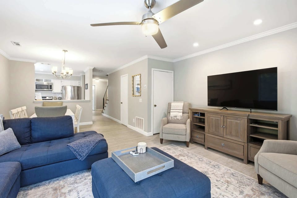Navy upholstery and light wood textures create a balanced, contemporary lounge. Bright recessed lighting and an open floor plan connect the plush seating area to the nearby kitchen for easy entertaining.
