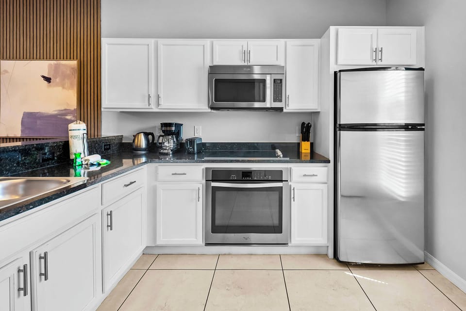 This kitchen boasts sleek stainless steel appliances and bright white cabinetry for a functional workspace. The rich dark countertops create contrast, while the elegant tiled floor enhances your culinary experience.
