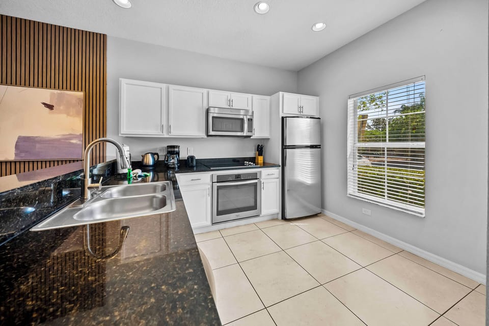 This bright kitchen boasts sleek white cabinetry and dark granite countertops for a stylish contrast. Natural light floods the space, highlighting modern appliances and inviting you to create your favorite meals with ease.