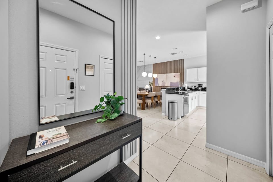 Welcome to a stylish entryway with sleek tile floors and a modern console featuring greenery. This open layout leads to a bright kitchen, where warm wood accents and pendant lighting create an inviting atmosphere for your stay.
