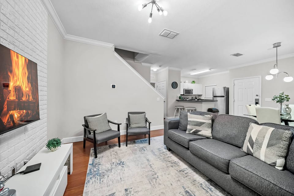 The cozy living area invites you to relax on a soft gray sofa with stylish armchairs, complemented by a modern electric fireplace that adds warmth, all set against light hardwood flooring that brightens the atmosphere.