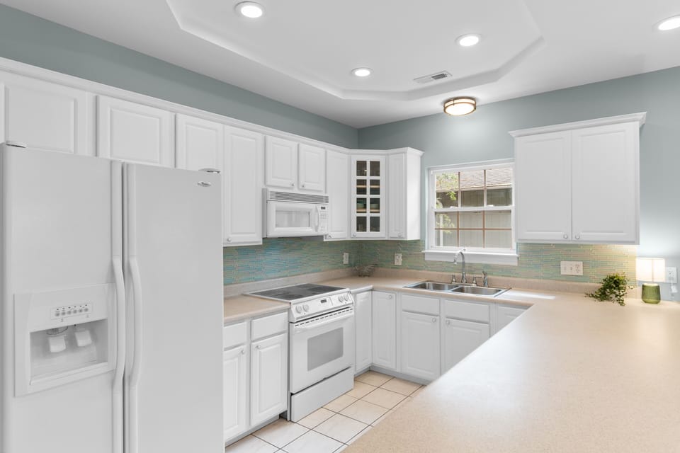 Picture yourself in this bright, fully-equipped kitchen with crisp white cabinetry, calming coastal-colored tile backsplash, and spacious counters perfect for preparing your favorite meals.
