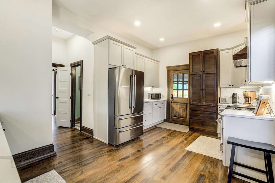 The main level kitchen features white shaker cabinets, hardwood floors, a stainless French door refrigerator, and a rustic barn-style door leading to the backyard, blending modern function with character-rich detail.