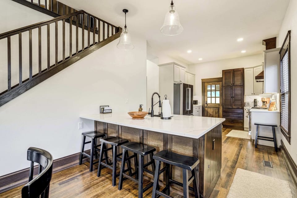 The kitchen island anchors the space with a light countertop, undermount sink, and four black bar stools, offering a casual dining and gathering spot that flows directly into the open main level.