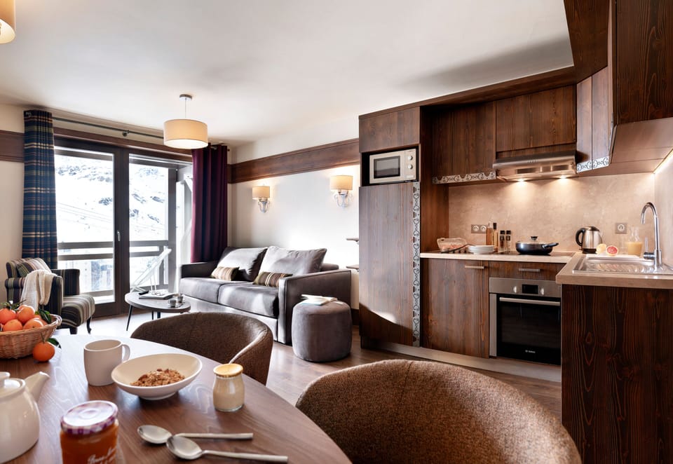 Fully equipped kitchen with dark wood cabinetry, ceramic hob, and dining table — everything you need for self-catering evenings at 2,300m.