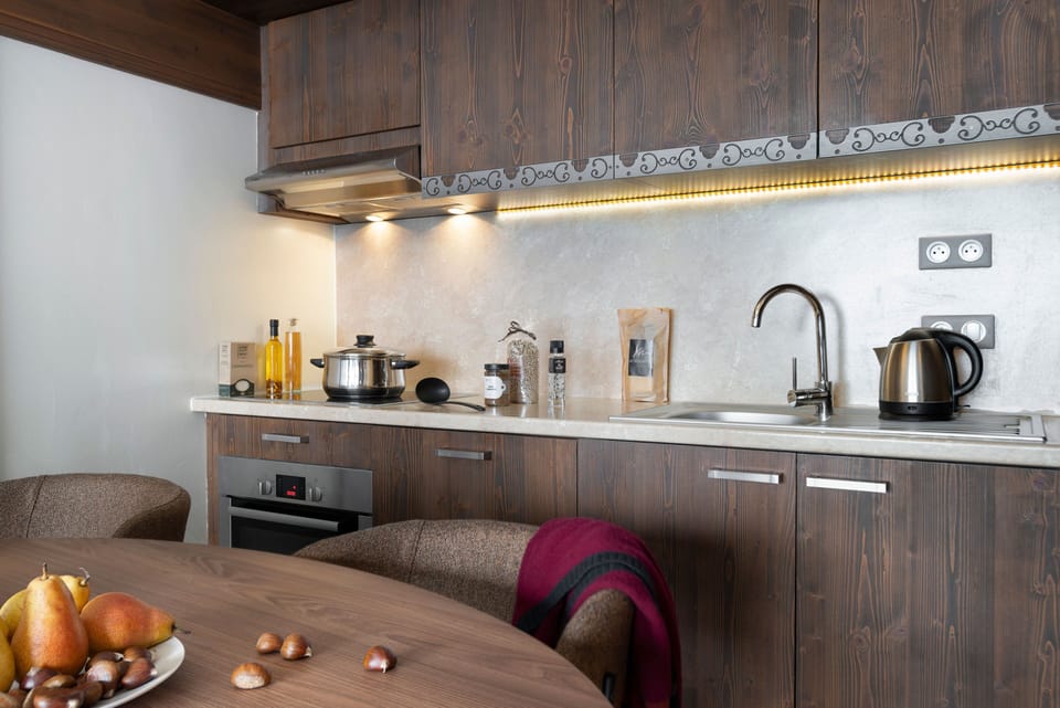 Dark wood kitchen with under-cabinet lighting, ceramic hob, Nespresso machine, and kettle — all you need before heading out on a morning hike.