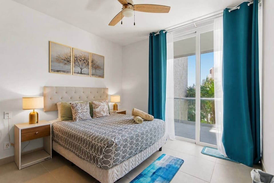 This bedroom features a comfortable queen bed with direct access to your private balcony, partial ocean views, and refreshing sea breezes. Includes A/C, a ceiling fan, bedside lamps, outlets, and light switches conveniently located next to the bed.