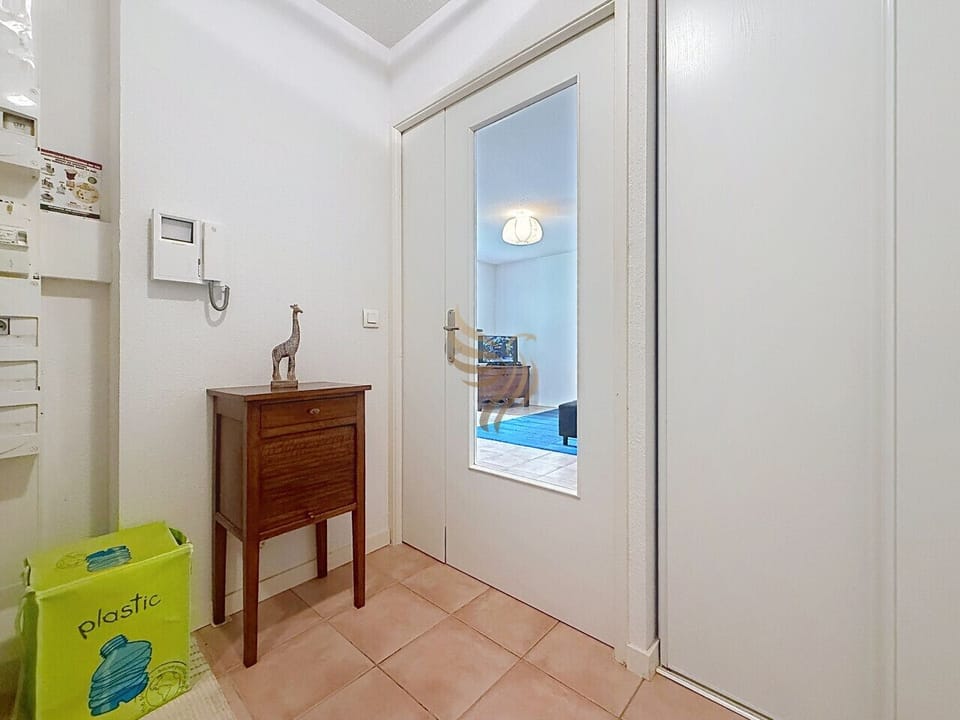 Posez vos clés sur la petite console en bois et laissez l`interphone annoncer votre arrivée. La porte vitrée laisse filer la lumière du salon : une entrée simple, lumineuse et accueillante.
