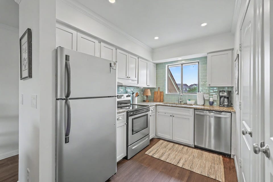 The fully stocked kitchen features modern stainless steel appliances, crisp white cabinetry, and a beautiful sea glass subway tile backsplash.