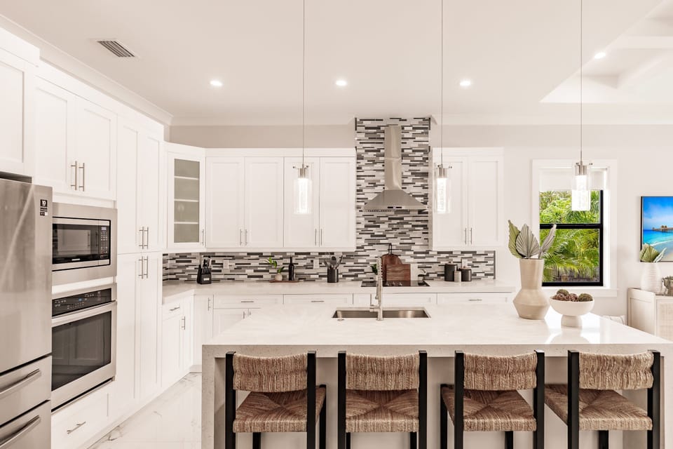 Gather around the oversized island in this bright chef’s kitchen featuring sleek finishes, ample prep space, and modern coastal style.