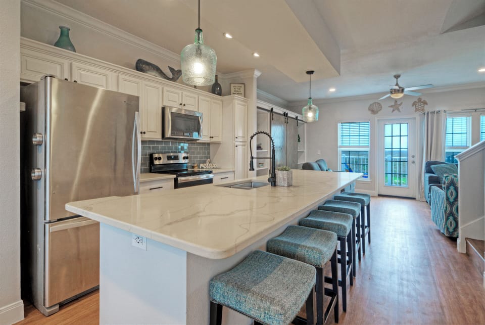 Cook, snack, and gather in the open kitchen with a large island, stainless steel appliances, and coastal styling.