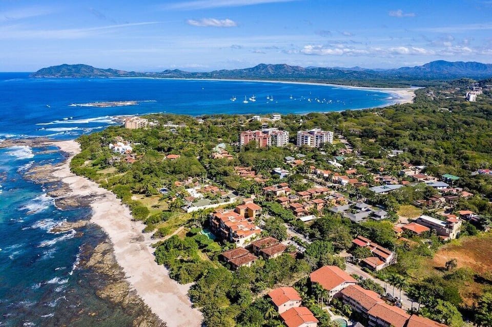 Aerial view of exclusive Playa Langosta neighborhood in Tamarindo area, Costa Rica. Upscale beach community, pristine coastline, tropical canopy, with famous Tamarindo beach visible in the background. Premium location for discerning travelers.