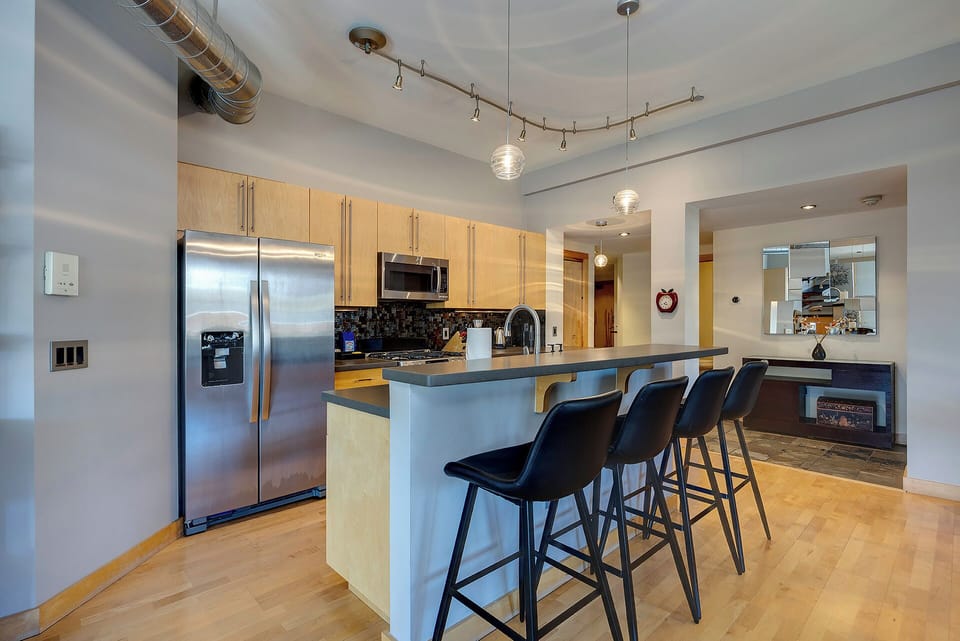 Step into a modern kitchen with sleek stainless appliances, warm wood cabinetry, and a stylish breakfast bar—perfect for your morning coffee or casual meals.