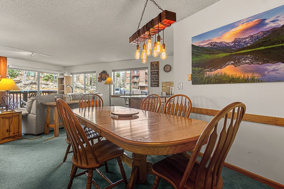 Gather around this inviting dining table for meals and stories beneath charming rustic lighting, with mountain views and cozy seating just steps away.