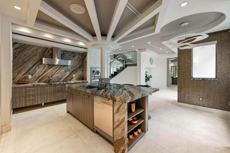 Sleek kitchen featuring rich marble finishes, large island, and open sightlines to the staircase