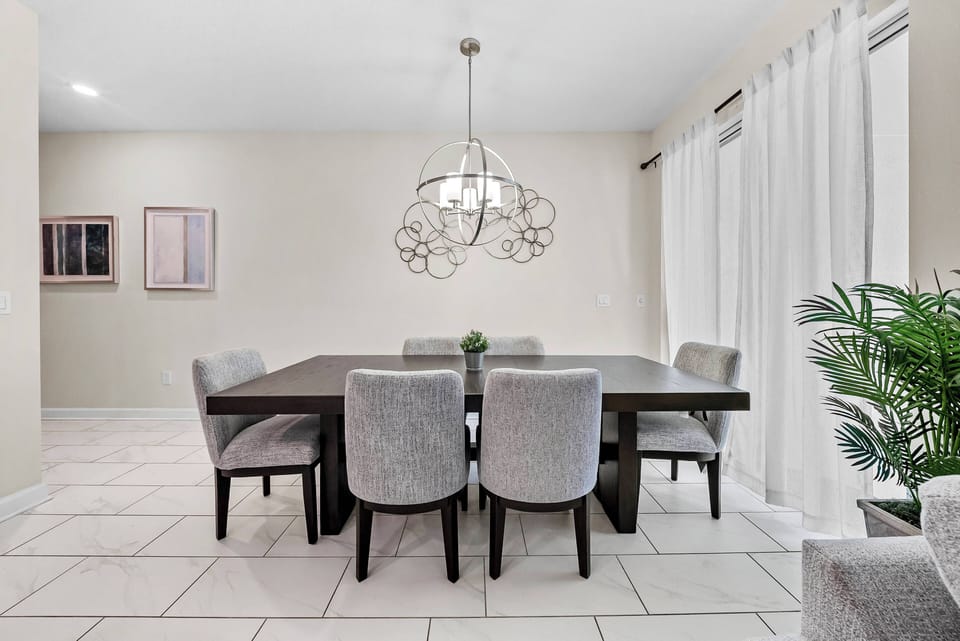 Enjoy enjoyable gatherings at the spacious dining table, surrounded by comfortable upholstered chairs. The warm glow of the modern chandelier enhances the elegant decor and tranquil color palette, creating a welcoming atmosphere.