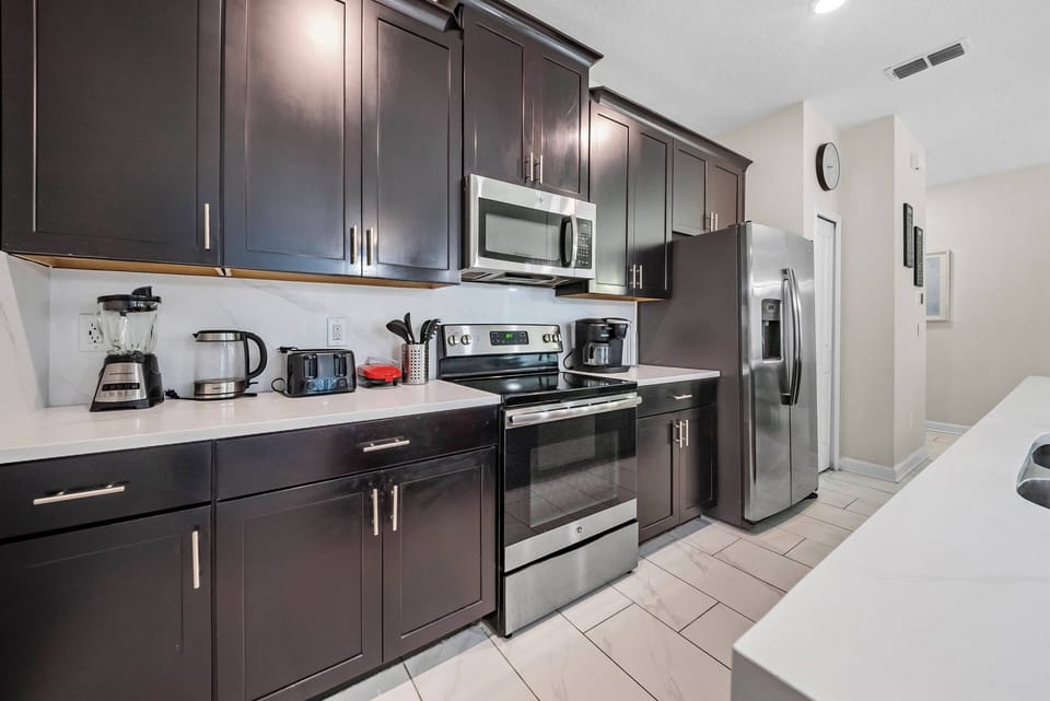 Indulge in a culinary experience in this stylish kitchen featuring dark cabinetry, stainless steel appliances, and a spacious countertop, blending modern design with functionality for an enjoyable stay.