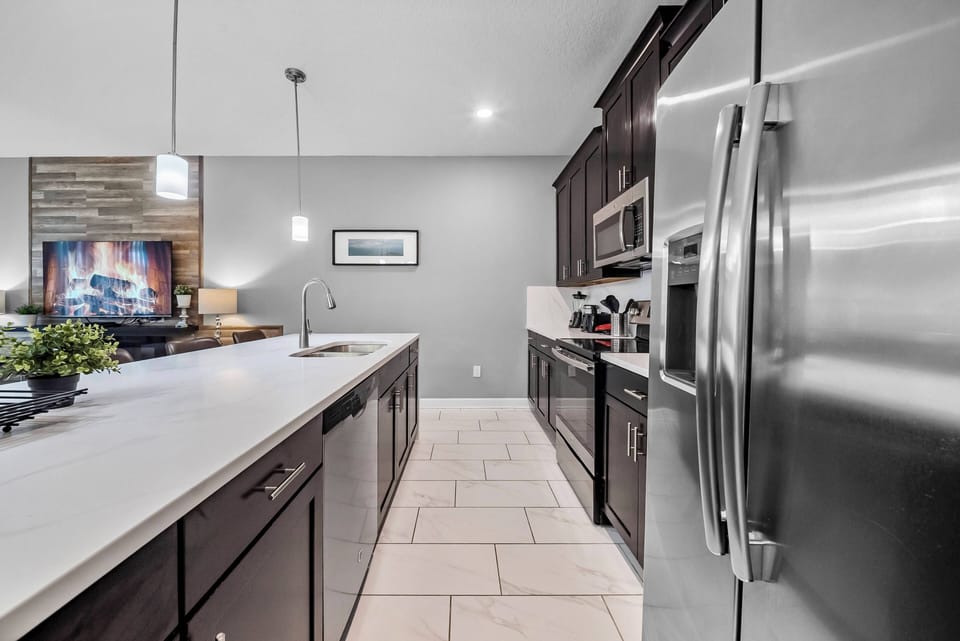 Welcome to this stylish kitchen featuring dark wood cabinets and stainless steel appliances. The spacious island sparks culinary creativity, while natural light highlights the elegant tile flooring, creating a warm and inviting.