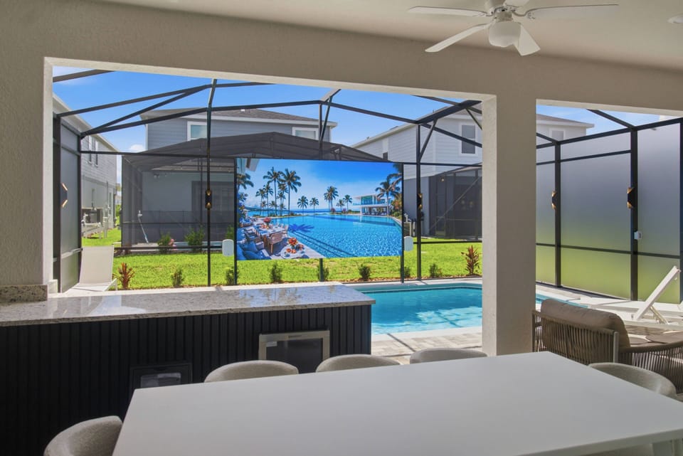 Step into a bright, airy space featuring a sleek dining table that overlooks a stunning pool area, accentuated by vibrant green grass. Enjoy cinematic evenings with a large outdoor screen, perfect for movie nights under the stars.