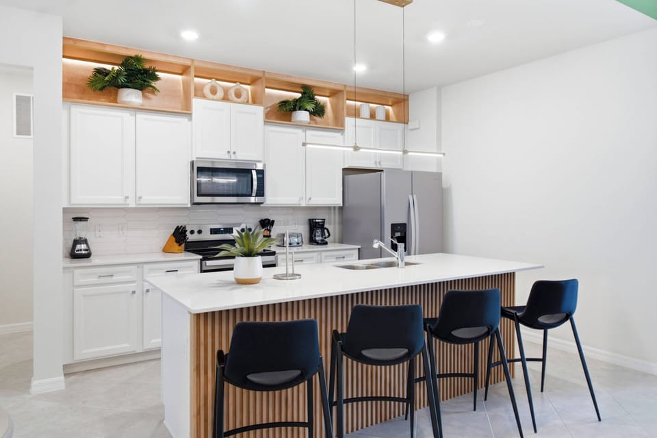 This stylish kitchen blends sleek white cabinetry with warm wooden accents, offering a fresh and functional space. Enjoy modern appliances and generous counter space while relaxing at the chic bar stools, ideal for casual meals.