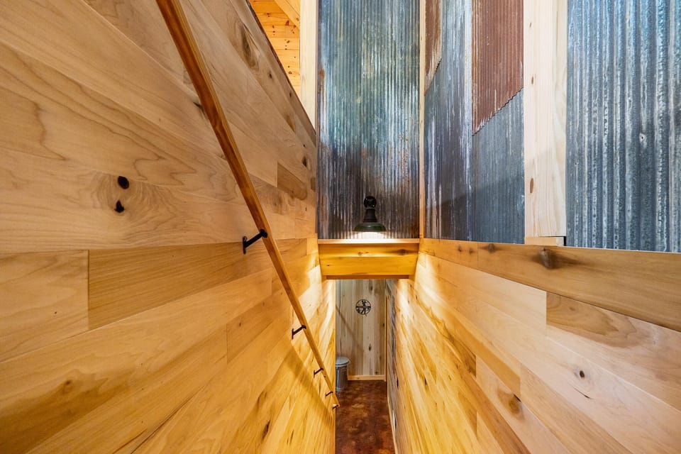 Narrow staircase with light pine wood paneling, corrugated metal accent walls, and a simple wooden handrail.
