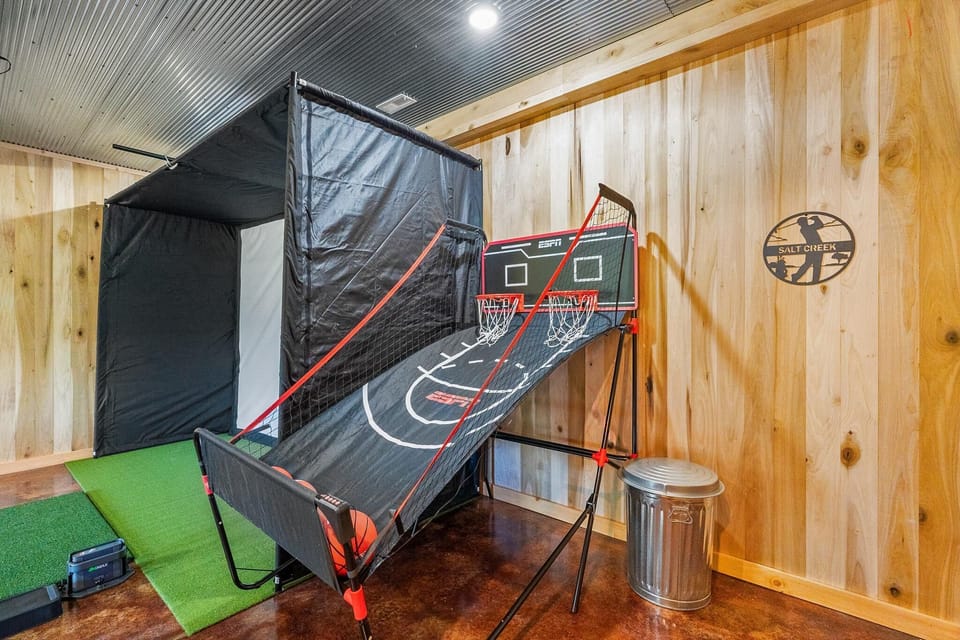 Game room corner with a dual hoop basketball arcade, polished concrete floor, and light wood-paneled walls.
