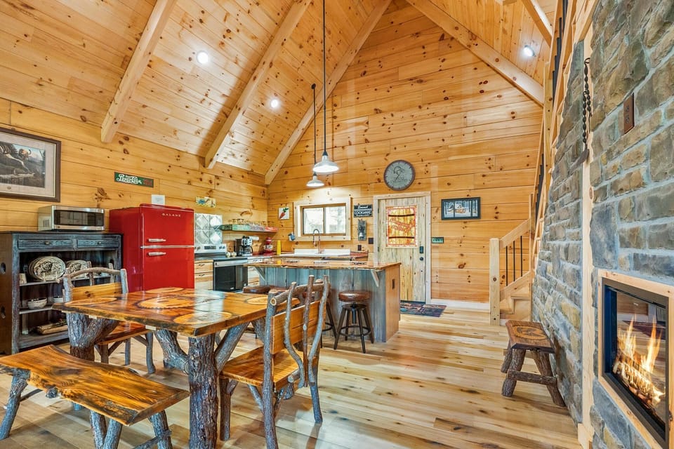 Open-concept kitchen and dining area with knotty pine walls, a red vintage fridge, and a stone fireplace.