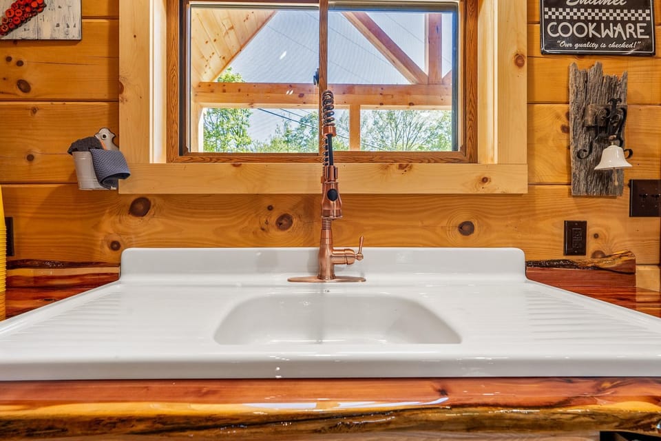 Kitchen sink with copper spring faucet set in a live-edge wood countertop beneath a window framed by natural pine walls.
