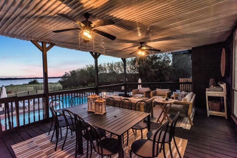 Dine and unwind on this covered lakefront patio, featuring outdoor seating for 12 people, warm lighting, and views of the pool and water just steps away.