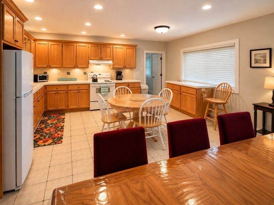 Cottage kitchen and dining area featuring a spacious wood table with vibrant red chairs and a full kitchen.