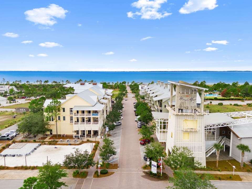 Aerial view of Windmark Beach with charming beach-style architecture, lush greenery, and the sparkling Gulf waters in the background—an inviting destination near the shore.