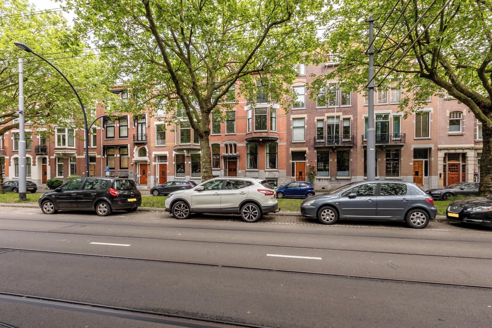 The apartment is located on Mathenesserlaan, a broad, tree-lined street in Rotterdam West with classic brick façades and tram connections directly in front of the building. The street is lively during the day but remains residential in character, with wide sidewalks and mature greenery. Shops, cafés, and public transport are all within easy walking distance.