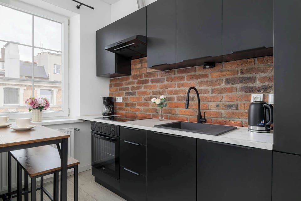 Modern black kitchen with wooden countertops and an exposed brick backsplash.