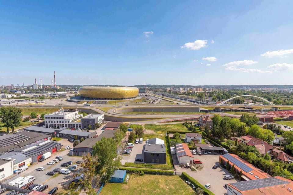 A wide panoramic view from the balcony looks out over a stadium and the urban landscape. The elevated perspective provides an impressive sight of the city's greenery and infrastructure.