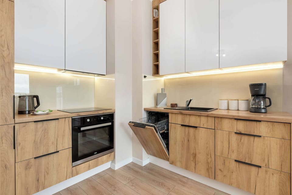 The kitchen setup includes a dishwasher tucked neatly between the wooden cabinets under a bright countertop. Integrated lighting beneath the upper cabinets provides excellent task lighting for food preparation.