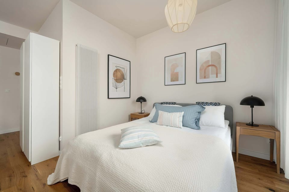 A beautifully arranged bedroom corner featuring a double bed with plush pillows and matching wooden nightstands on either side. Symmetrical artwork above the bed enhances the cohesive design.