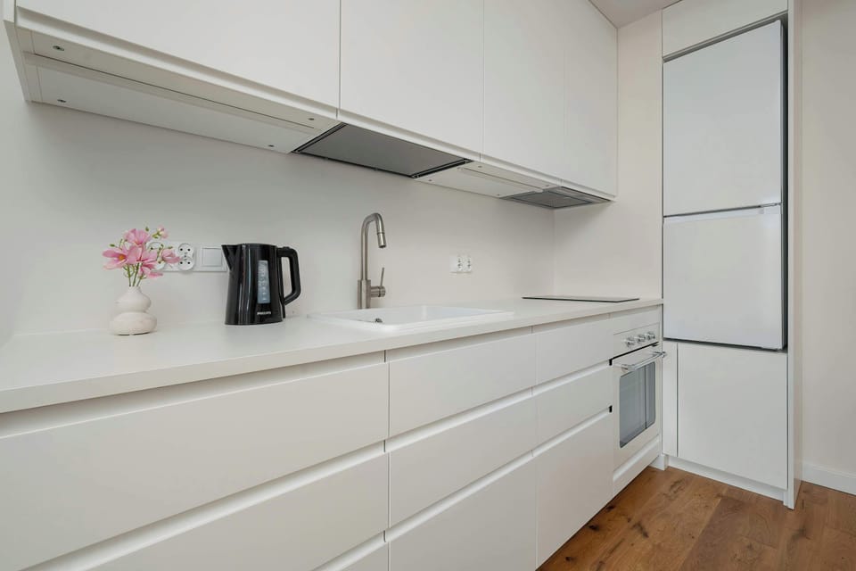 A close-up shot of the pristine white kitchen counter with a built-in sink and a modern chrome faucet. The clean lines emphasize the high-end, functional design of the cooking area.