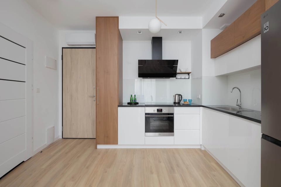 A modern kitchenette with white cabinets, wooden accents, and built-in appliances. The bright interior feels clean and spacious.