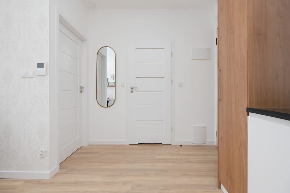 A bright hallway with white doors, wooden details, and a large mirror. The simple design creates a welcoming atmosphere.