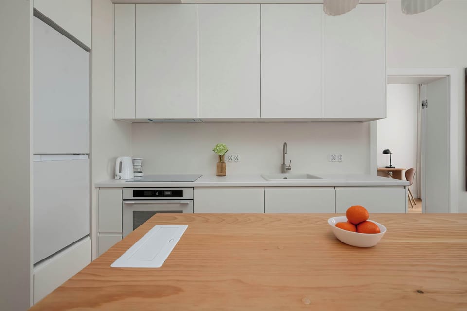 A sleek kitchenette with white cabinets, built-in appliances, and a wooden countertop.