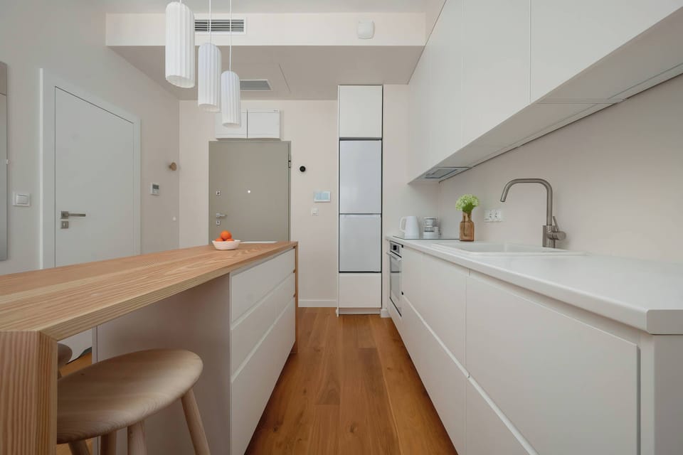 A narrow modern kitchen with clean lines, light cabinetry, and wooden accents.