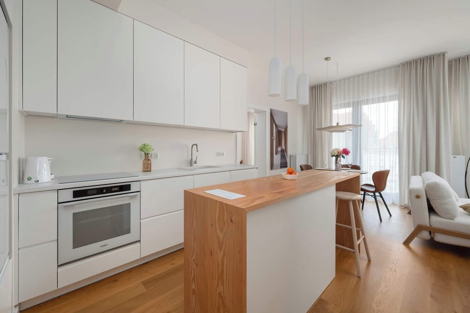 A modern kitchenette with white cabinetry, wooden countertops, and a compact dining area nearby.