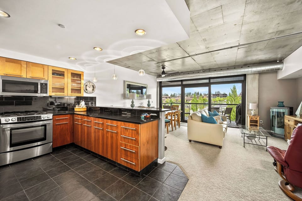 Your open-concept space merges modern comfort with industrial chic, where sleek wood cabinetry, polished countertops, and stainless appliances invite culinary creativity while natural light floods in from the private balcony.